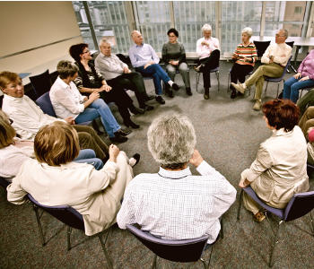 A large group of 17 people gather in a support group. They are seated in a circle. 