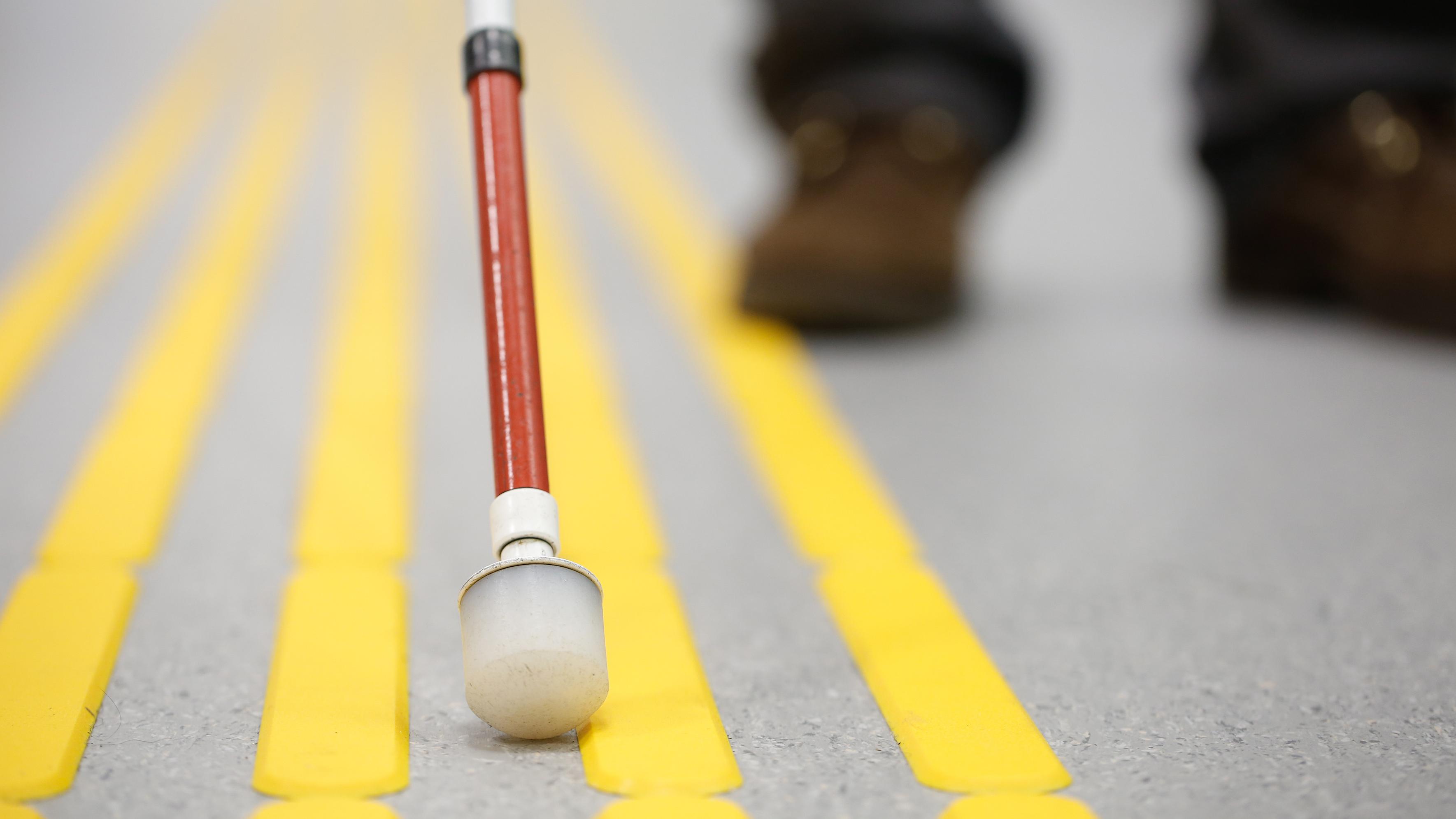 A white cane being used on pavement with raised yellow lines.
