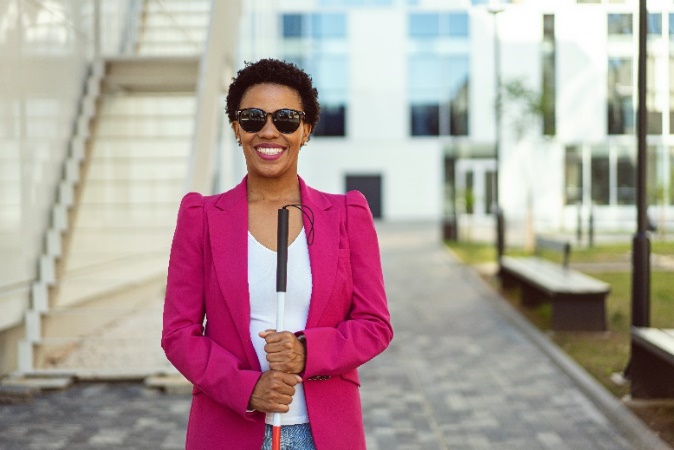 Smiling woman wearing blazer and sunglasses holds white cane.