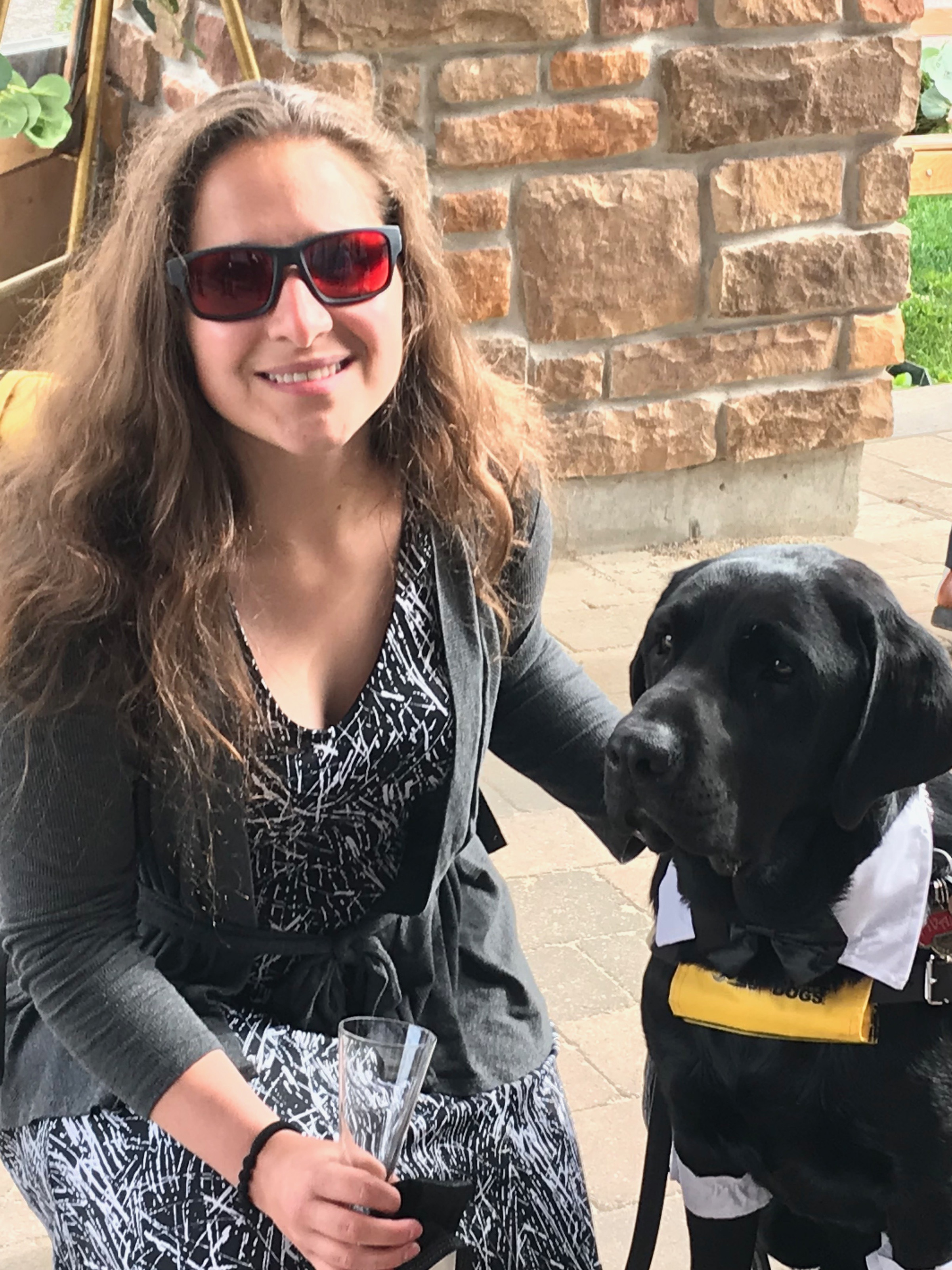 Amanda, agenouillée à lAmanda, agenouillée à l’extérieur et portant des lunettes de soleil teintées de rouge, pose pour la caméra à côté d’Ivan, son chien-guide d’INCA.