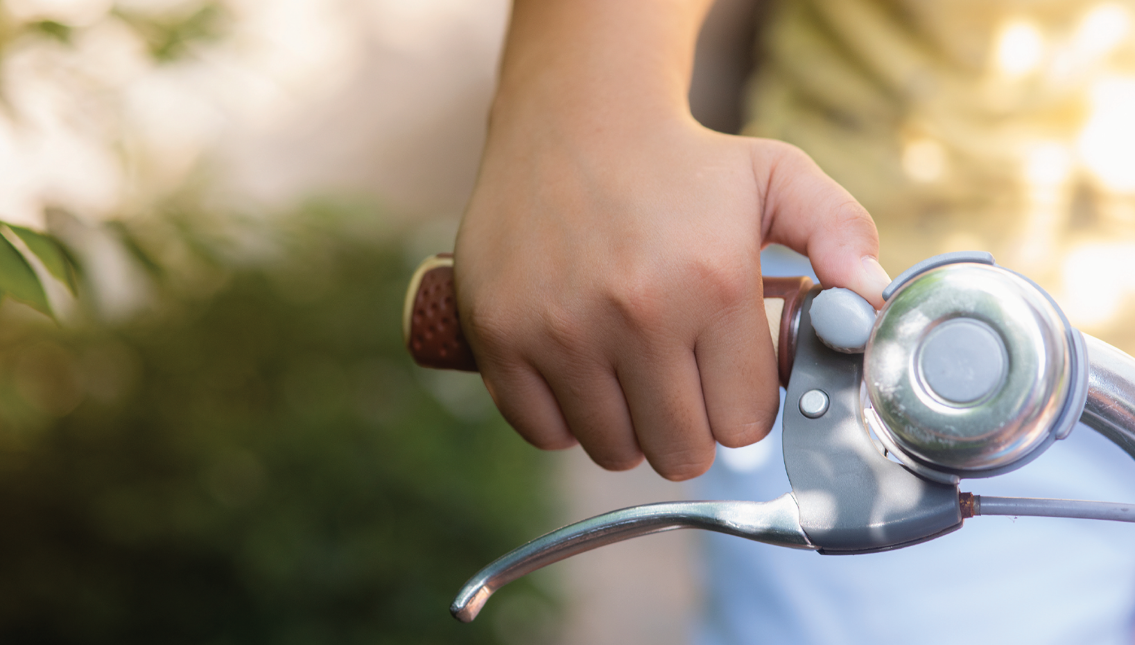 A person’s hand rings a silver bicycle bell. The bell is mounted on the bicycle handlebar. 