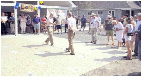 A photo of a celebration at Lake Joe. Two walk to shake hands in front of a  gathered crowd. 