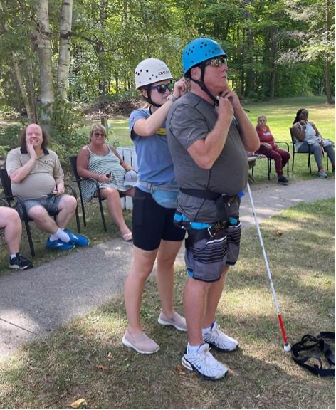 A staff member helps secure a helmet for a guest standing at the base of the climbing tower at Lake Joe.