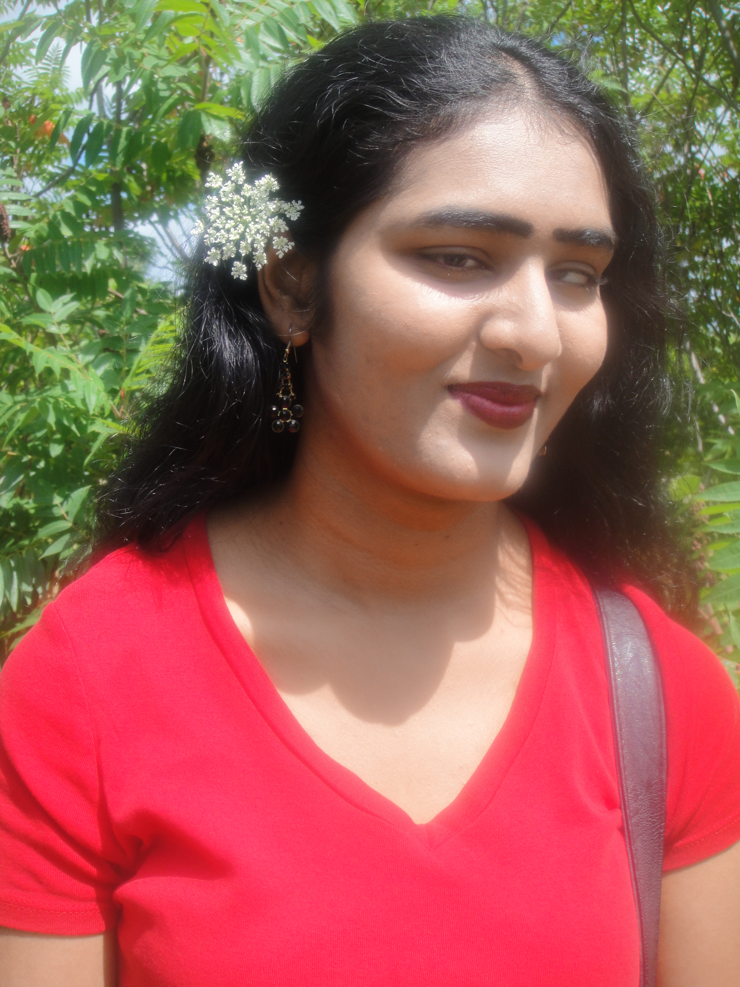 Portrait de Kamini, souriante, portant un haut rouge à col en V et une fleur blanche dans les cheveux