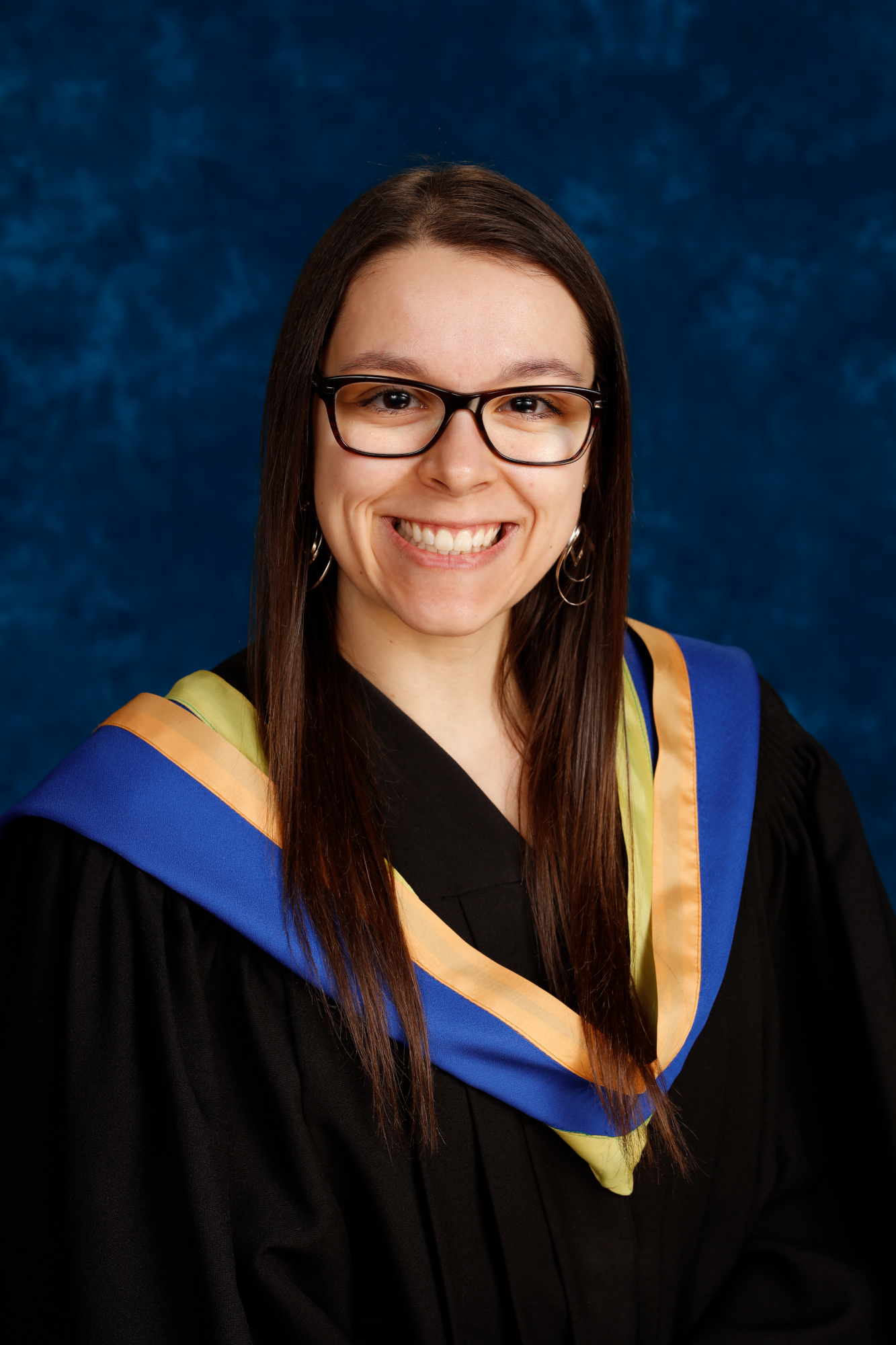 A graduation photo of Danica Frappier. She is smiling and wearing a graduation gown with a stole in blue, yellow and gold accents.