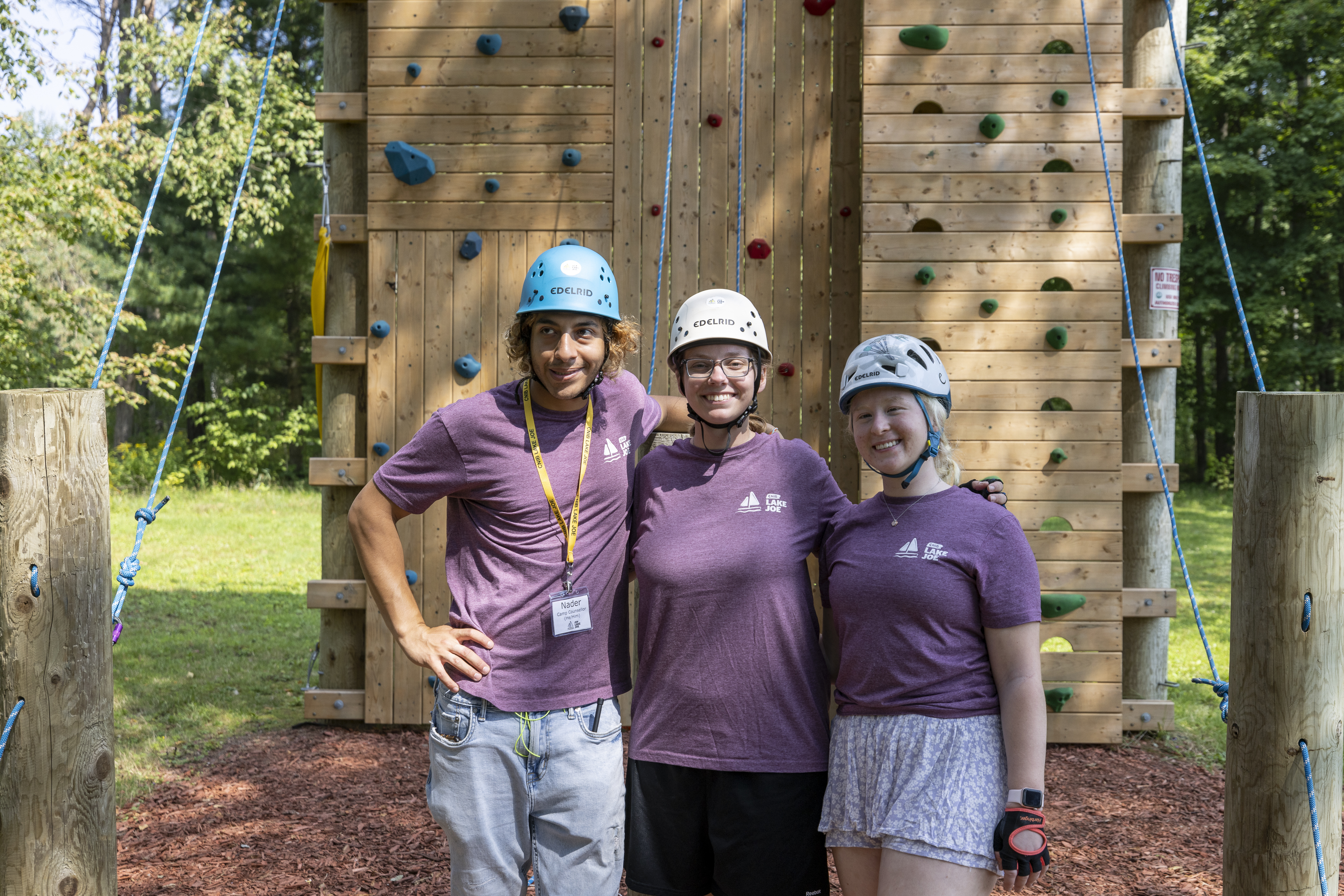 Three camp counsellors stand in front of the climbing tower