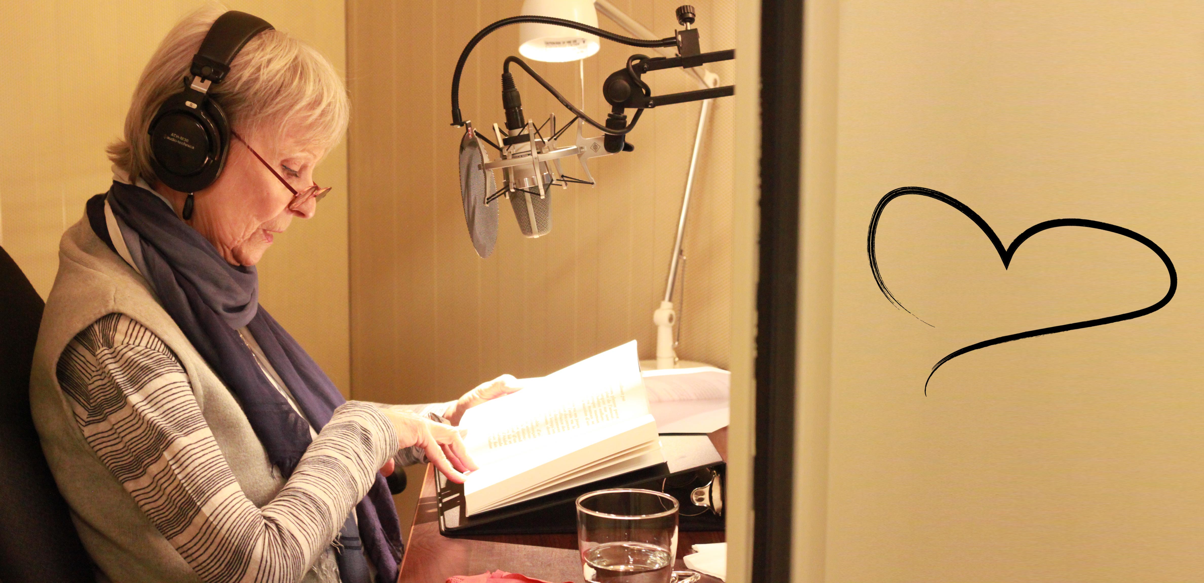 Celine Garneau, reading from a book in one of CNIB’s recording studios. A heart graphic can be seen on the wall in the right side of the picture