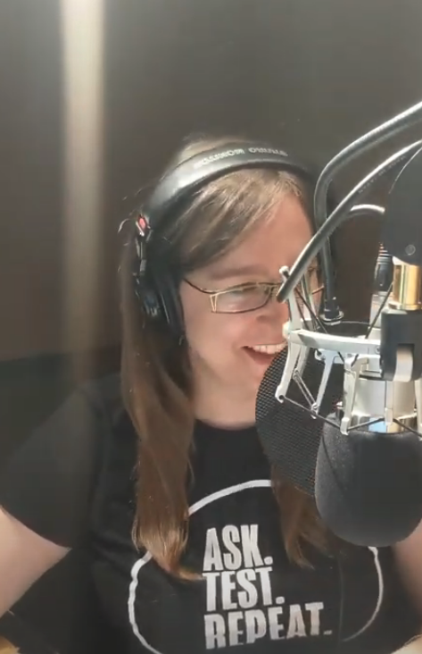 Dana est assise dans une cabine d'enregistrement. Elle porte un gros casque d’écoute et parle dans un microphone. 