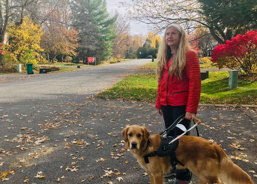 Diane Bergeron marche avec son chien-guide, Carla. Carla porte un harnais et se tient à sa gauche.