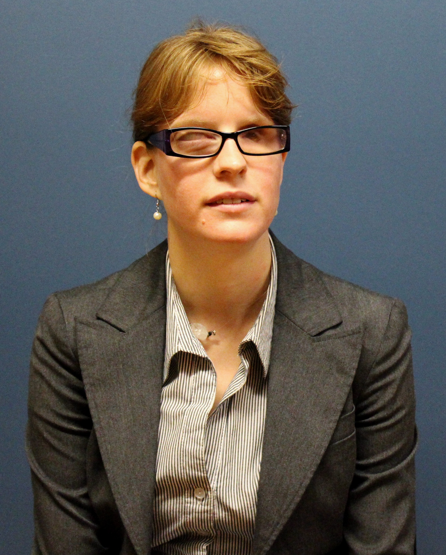 Elizabeth standing against a dark background wearing professional clothing and smiling for the camera.