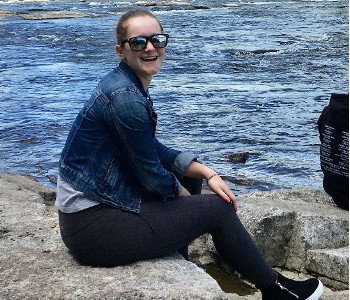 Emilee assise sur un rocher au bord de l'eau avec un grand sourire sur le visage. 