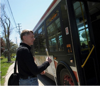 A man holding a white cane who's about to board a city bus.