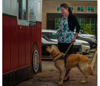 Larissa devant un camion de cuisine de rue avec Piper – un chien-guide Golden Retriever portant un harnais jaune. 