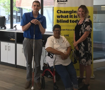 Ryan Hooey pose pour une photo au Hub de London avec Kristeen Elliott, membre de la communauté des personnes sourdes-aveugles et ambassadrice des Services communautaires surdicécité d’INCA et Christine, une interprète pour personnes sourdes-aveugles. 