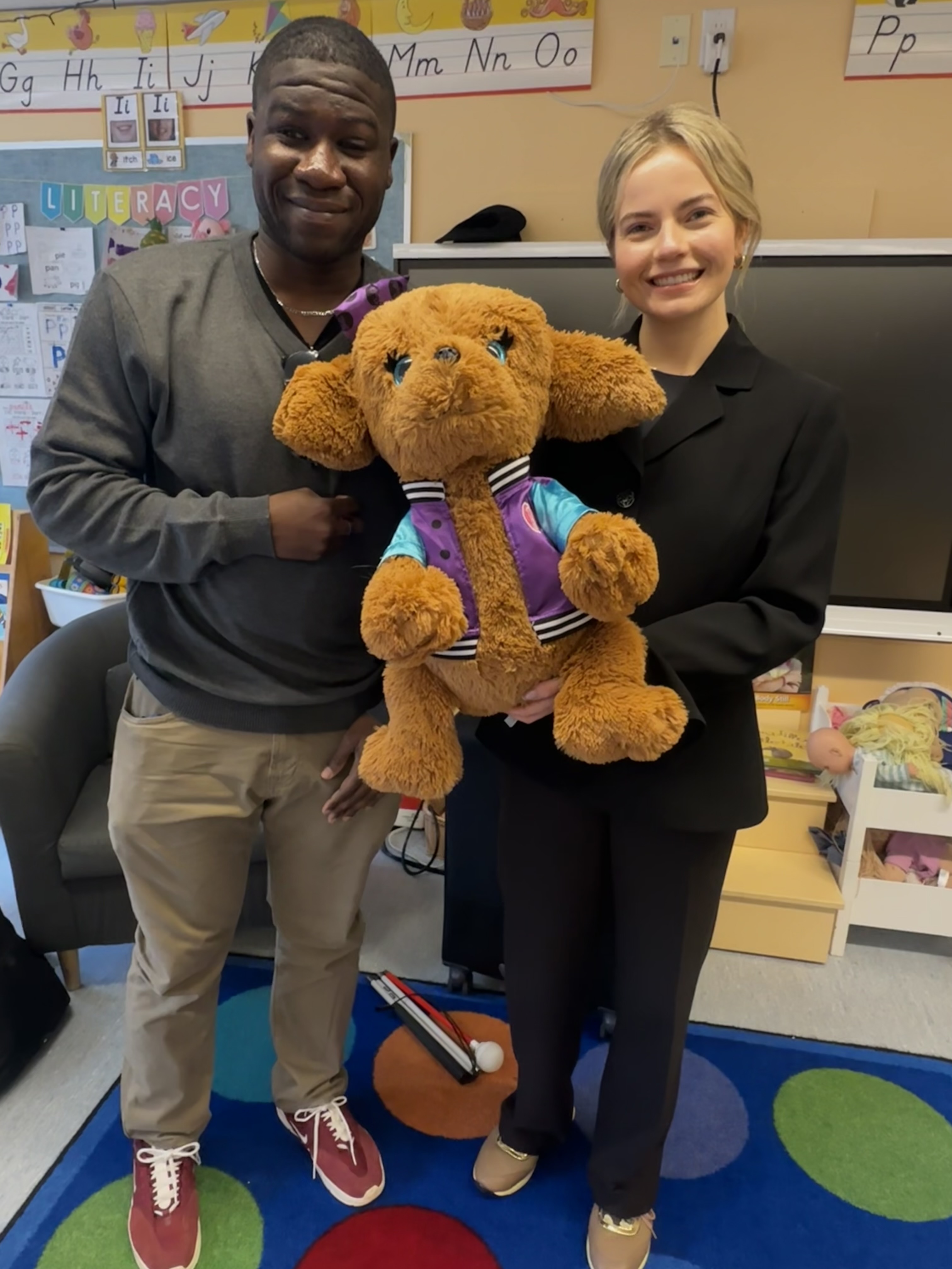 Ben and Martina from CNIB standing at the front of the classroom holding a CNIB guide dog plushy.