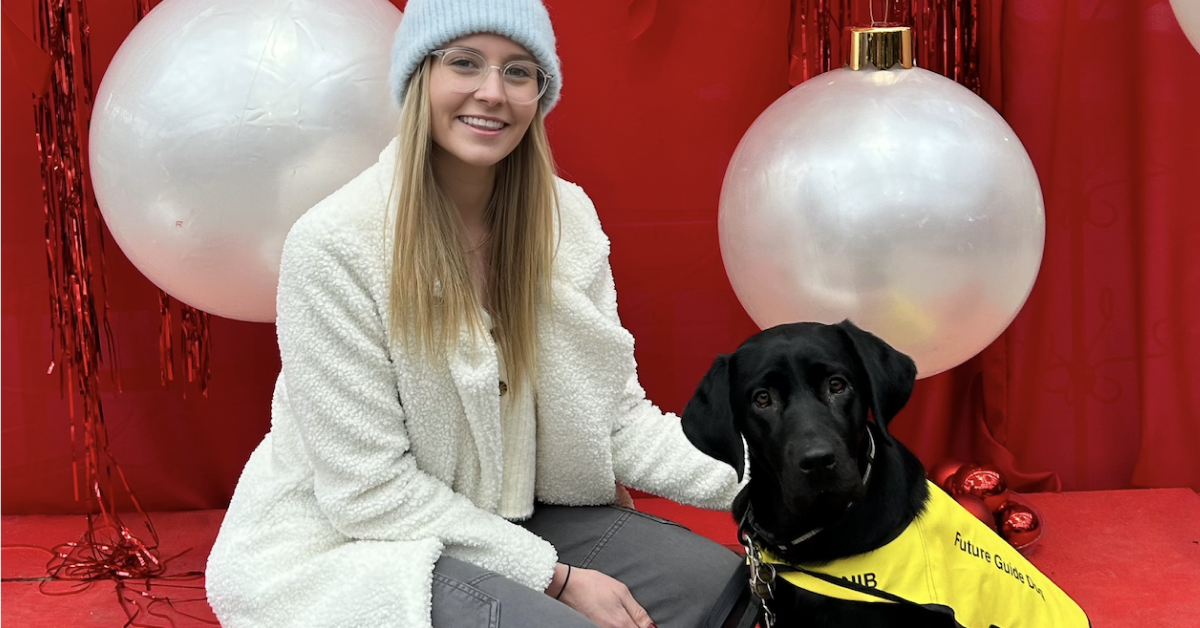 Hannah Guttormson, a CNIB Guide Dog Puppy Raiser, poses with her black Labrador puppy, Bambi, at a special event. Bambi wears her yellow CNIB Guide Dog vest.