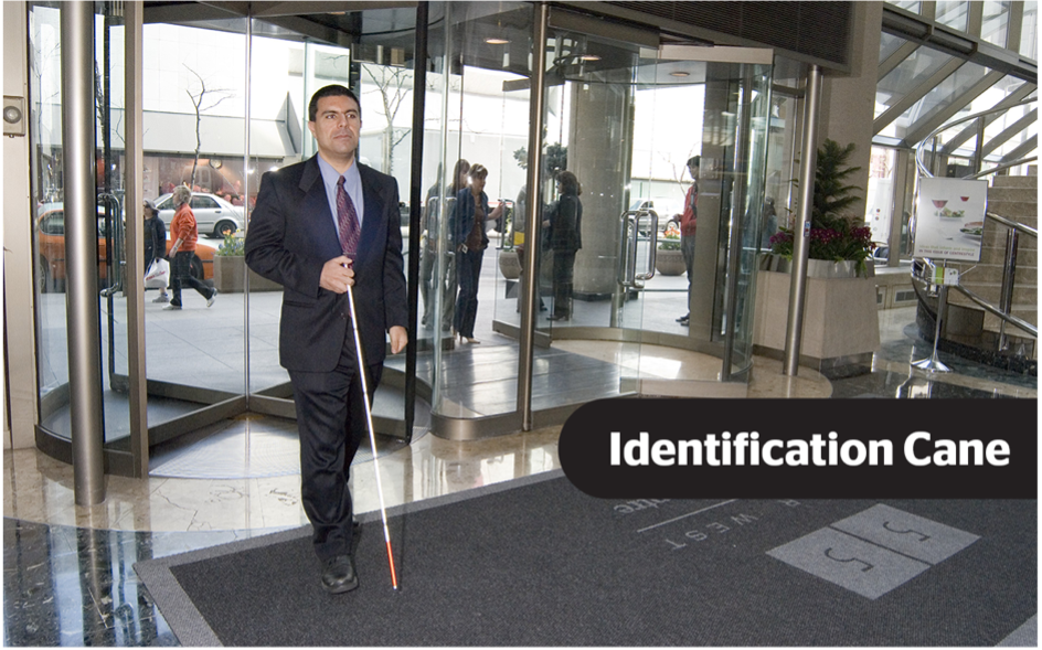 Un homme portant un costume entrant dans le hall d'un immeuble de bureaux à l'aide d'une canne d'identification. Les mots « Canne d'identification » sont superposés en texte blanc sur un fond noir.
