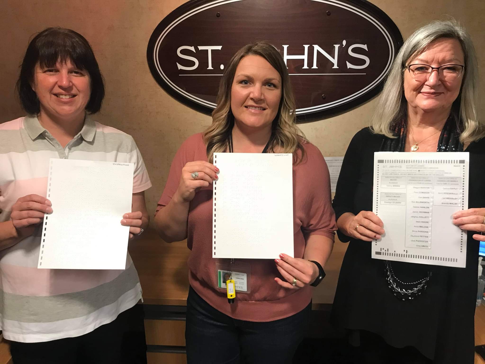 Kim Hart, INCA, Trisha Rose, coordonnatrice des élections de la ville de St John, et Debbie Ryan, INCA, tenant le premier bulletin de vote en braille utilisé lors des élections municipales de 2021.