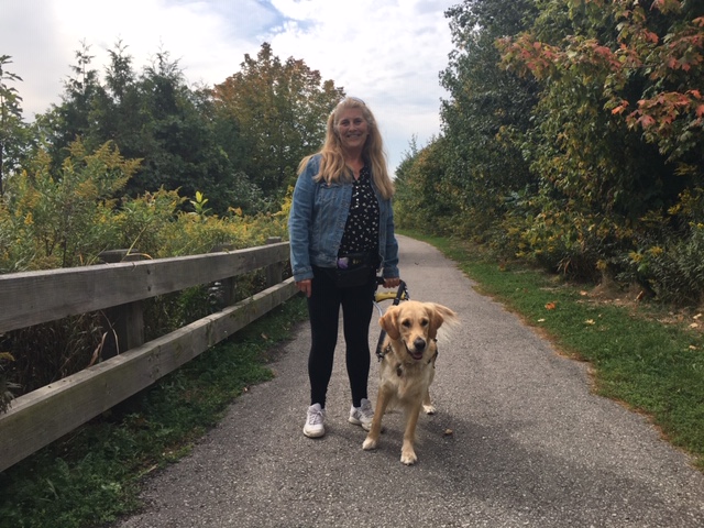 Photo of Lindsay and Charlie walking along a pathway in a park on a sunny day, smiling for the camera.