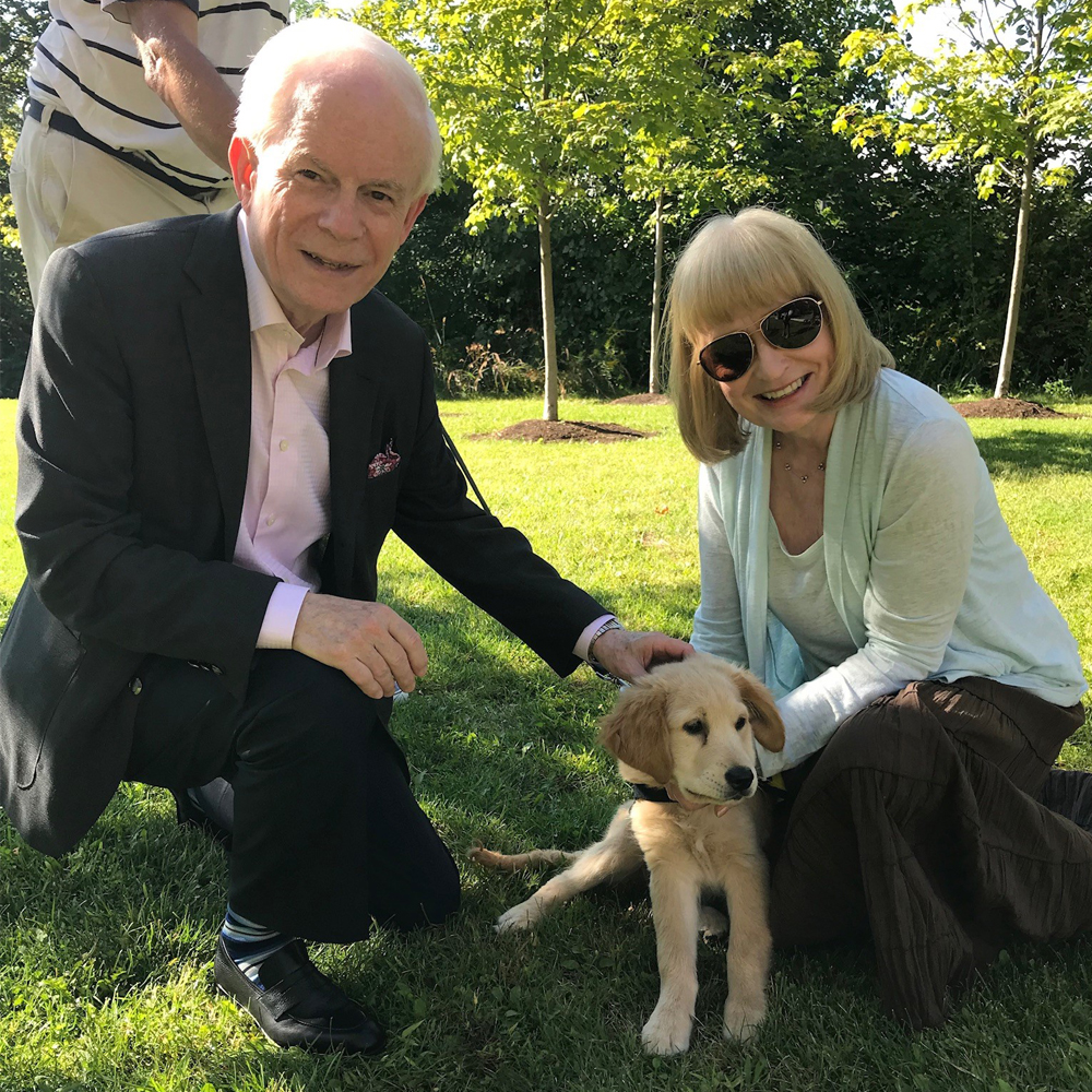 A man and woman smiling with a Golden Retriever puppy on the grass.