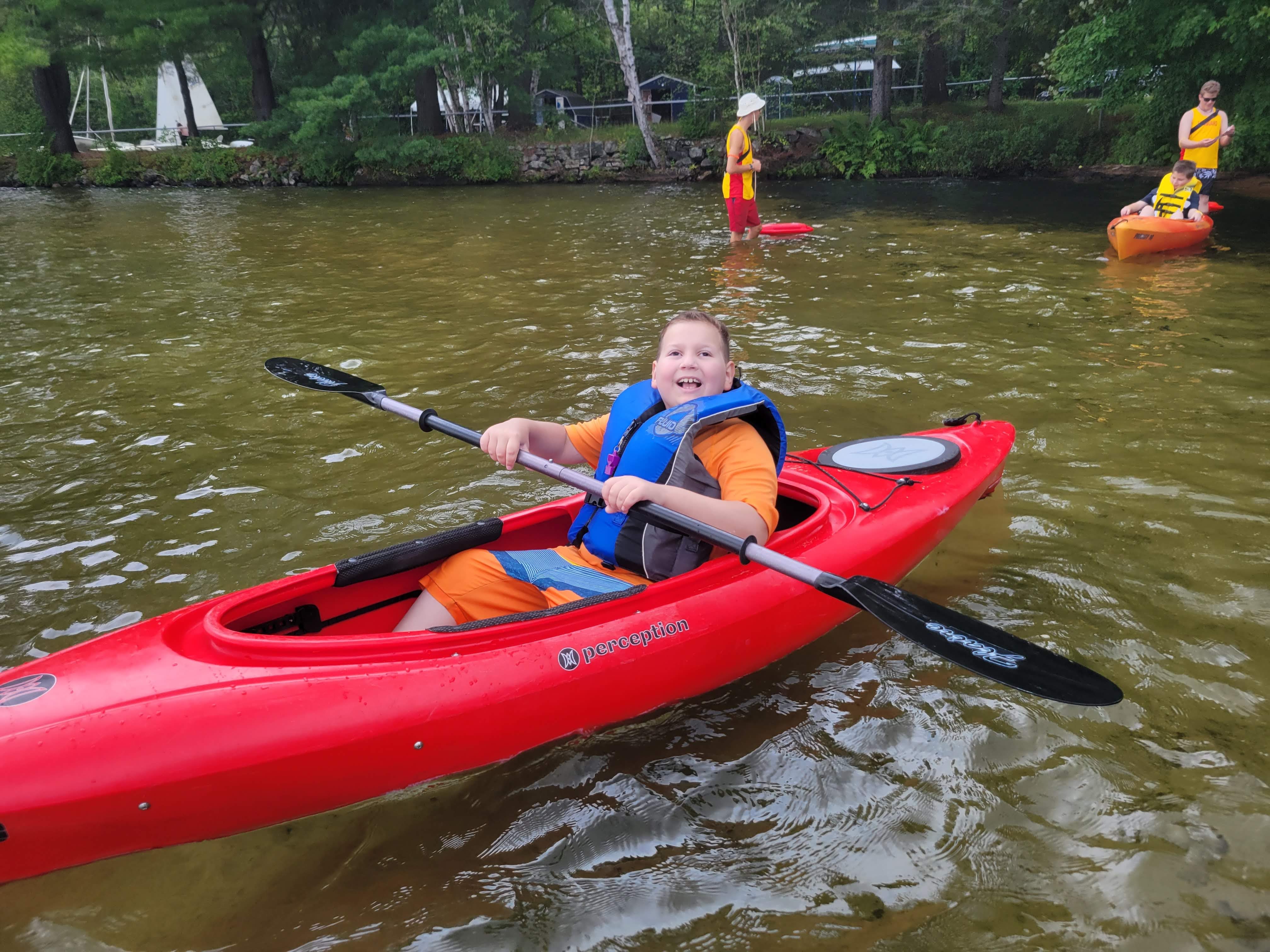 Ollie sits in a red kayak in the lake at CNIB Lake Joe.