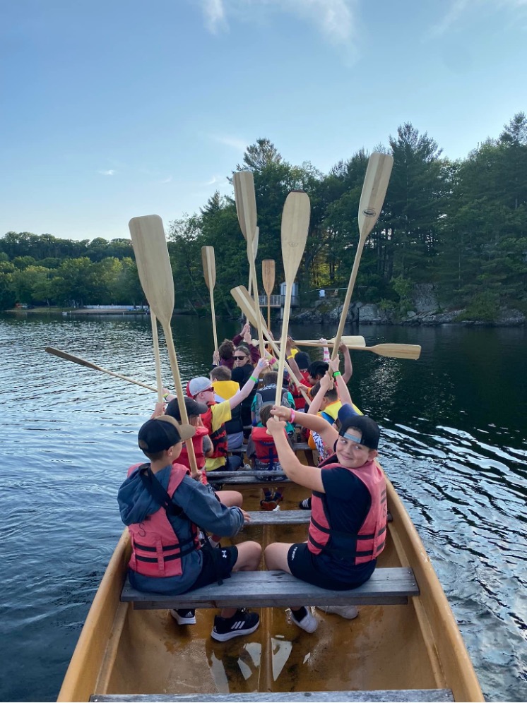 Canoeing on lake joe! Children and youth sit in the Voyageur canoe and hold their paddles high up in the air. 