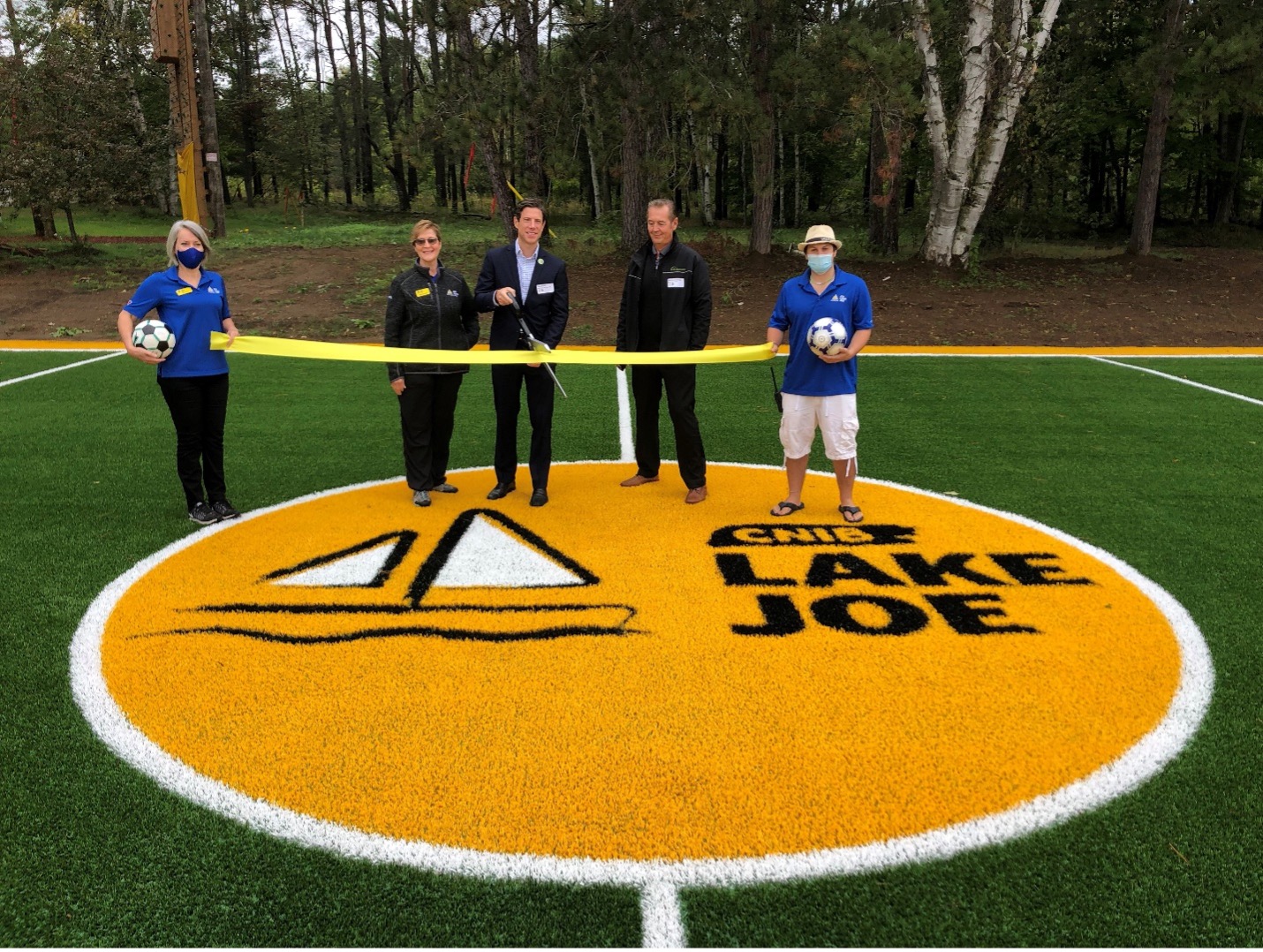 Coupure de ruban sur le nouveau terrain de soccer du camp Lake Joe d’INCA. De gauche à droite : Sherri et Monique (du camp Lake Joe d’INCA), Dan et Mark (du Synthetic Turf Council) et Josh (du camp Lake Joe d’INCA).