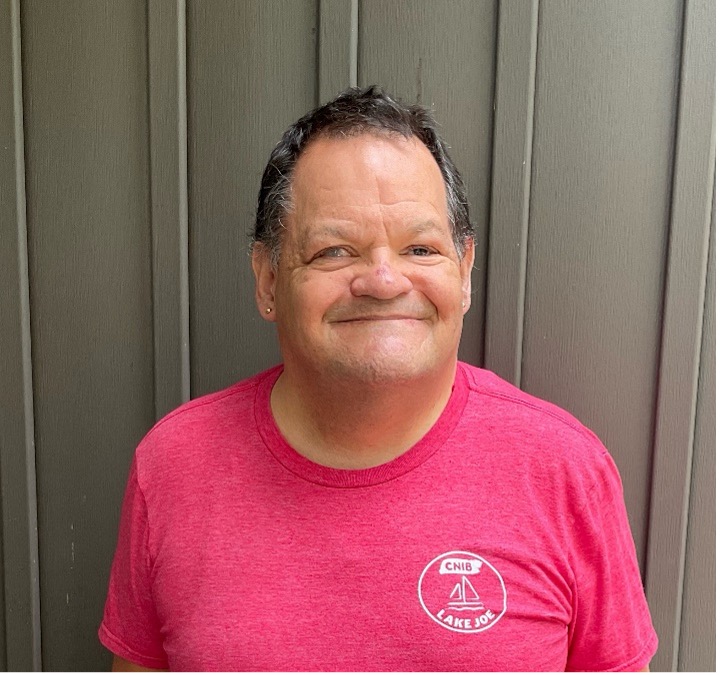 Photo de Shawn tout sourire, portant un tee-shirt rouge du camp Lake Joe d’INCA. 