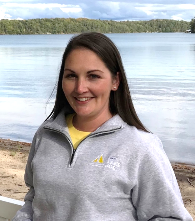 Lindsay Garrett, gestionnaire de programme, se tient sur la plage de Lake Joe et porte un sweat-shirt gris à fermeture éclair trois-quarts. 