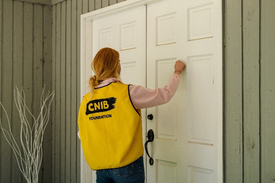 Un collectrice de fonds portant sa veste jaune d’INCA cognant à une porte.