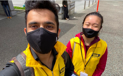 Deux collecteurs de fonds d'INCA souriants, portant un masque et leur veste jaune.