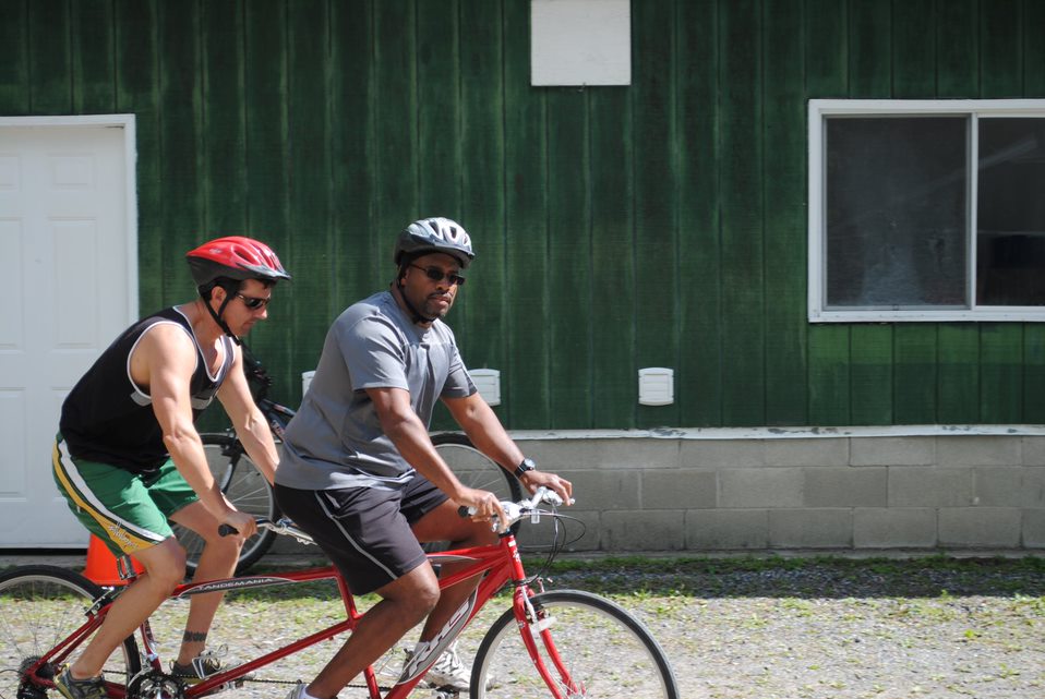 Derek Thompson and Shawn Dale ride a red tandem bicycle at CNIB Lake Joe. 