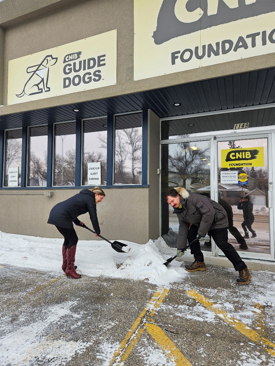 Amanda Titman et Dallas Lynch, membres du personnel d'INCA et de RDVC, utilisent les pelles de la campagne « Déneiger la voie! » pour déneiger un emplacement de stationnement accessible devant le bureau d'INCA à Saskatoon. 