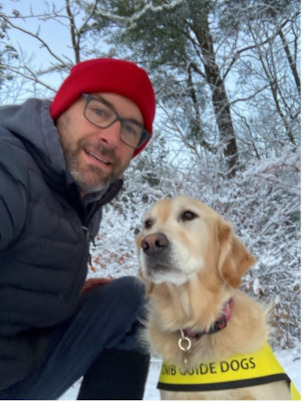 Barry agenouillé dehors dans la neige à côté de Willow qui porte sa veste de chien-guide d'INCA.