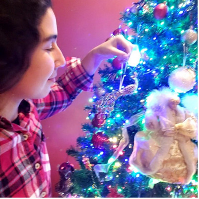 Diane accrochant un ornement sur un arbre de Noël entièrement décoré.