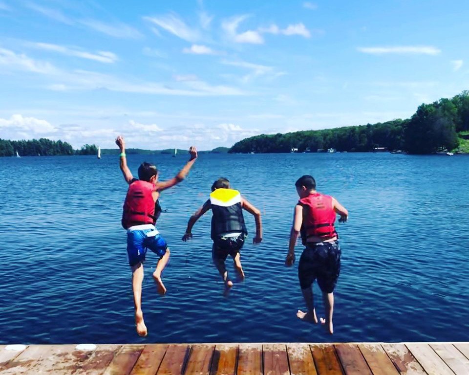 Trois jeunes garçons portent des gilets de sauvetage et sautent du quai dans le lac à INCA Lake Joe.