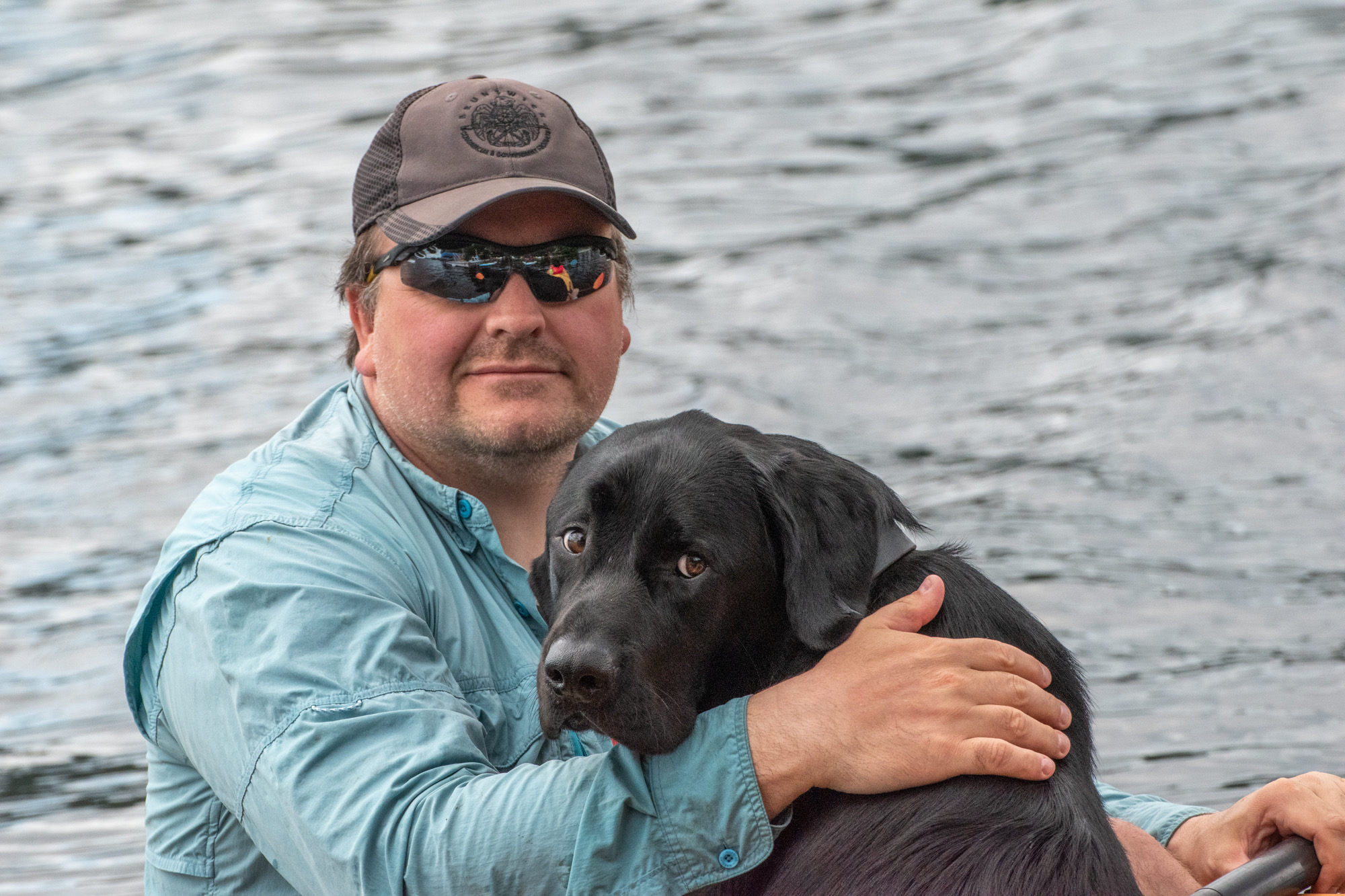 Photo de Tim et de son chien-guide Harlow, assis dans un bateau avec l'eau en arrière-plan.