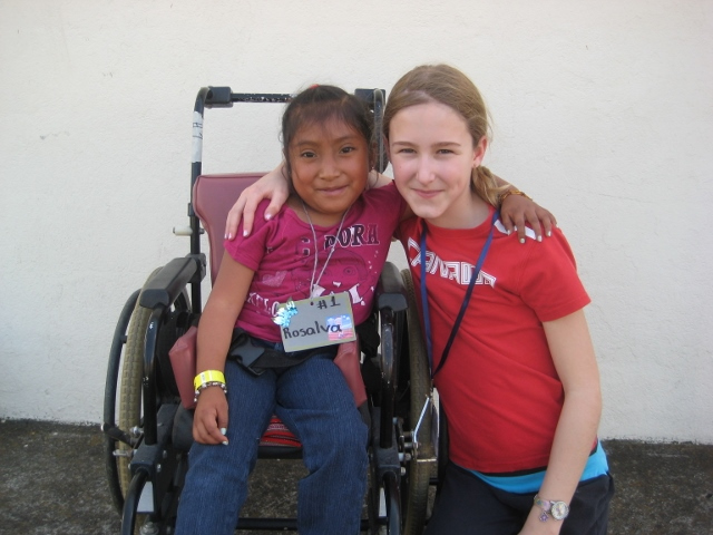 Au Guatemala, une jeune Veronika s'accroupit à côté d'une jeune fille en fauteuil roulant. Elles se tiennent par le bras et posent pour la photo. 