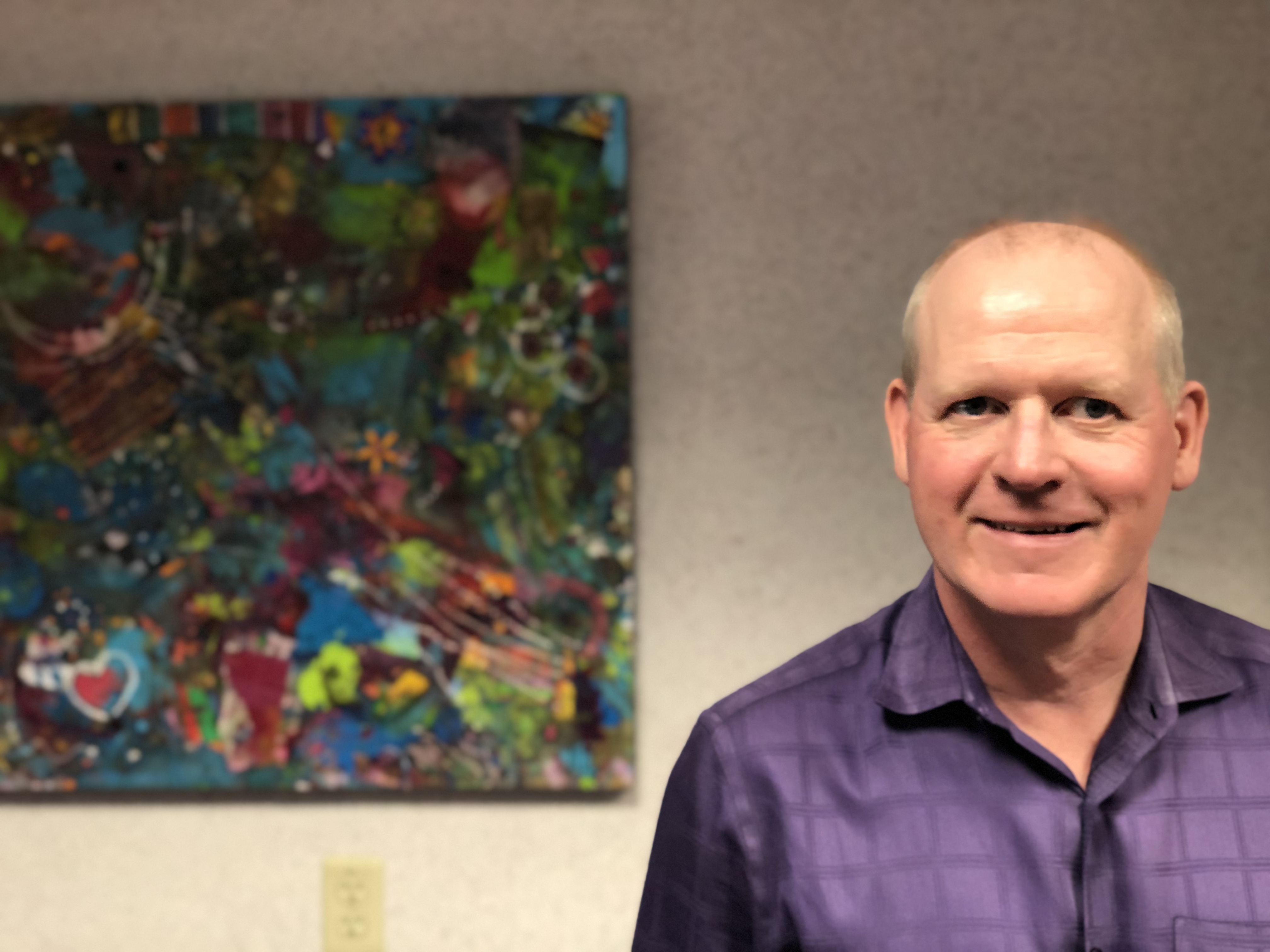 Christopher Warner smiles and stands beside an abstract painting at the CNIB office in Calgary.