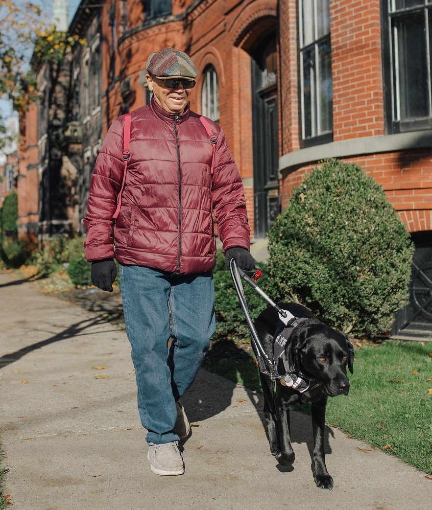 Blair walks with his CNIB guide dog, Kelly, a black Labrador retriever.