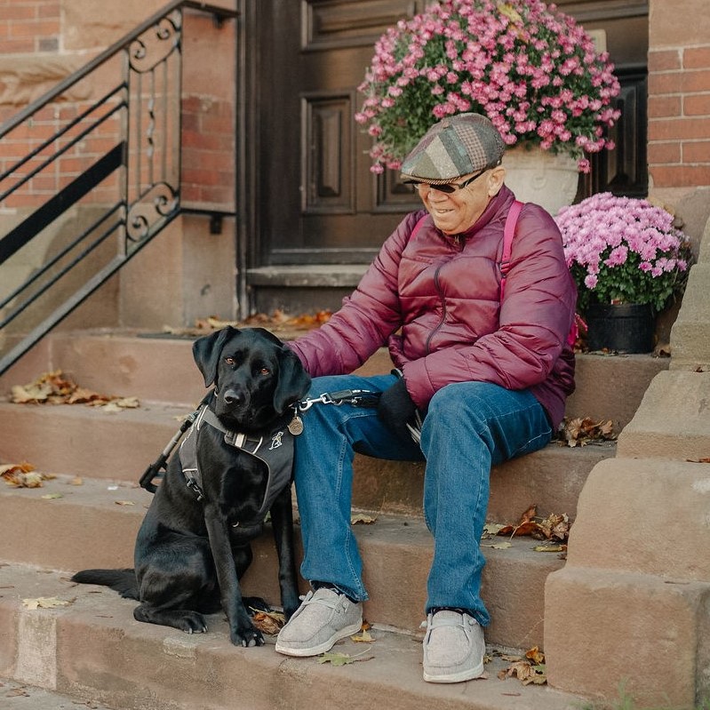 Blair is beside his CNIB guide dog, Kelly, a black Labrador retriever.