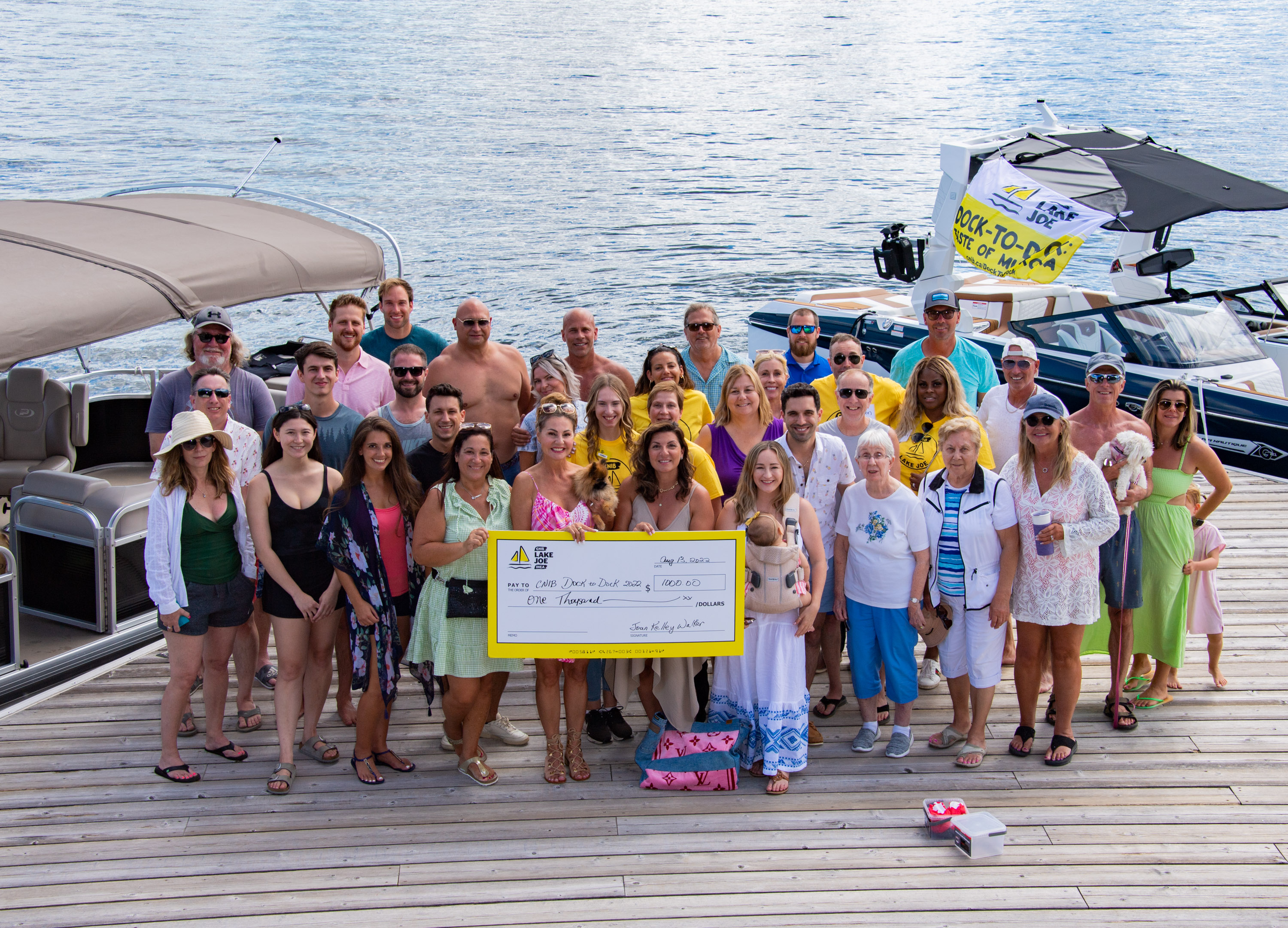 Guests on dock smiling and waving at the camera holding a yellow novelty cheque.