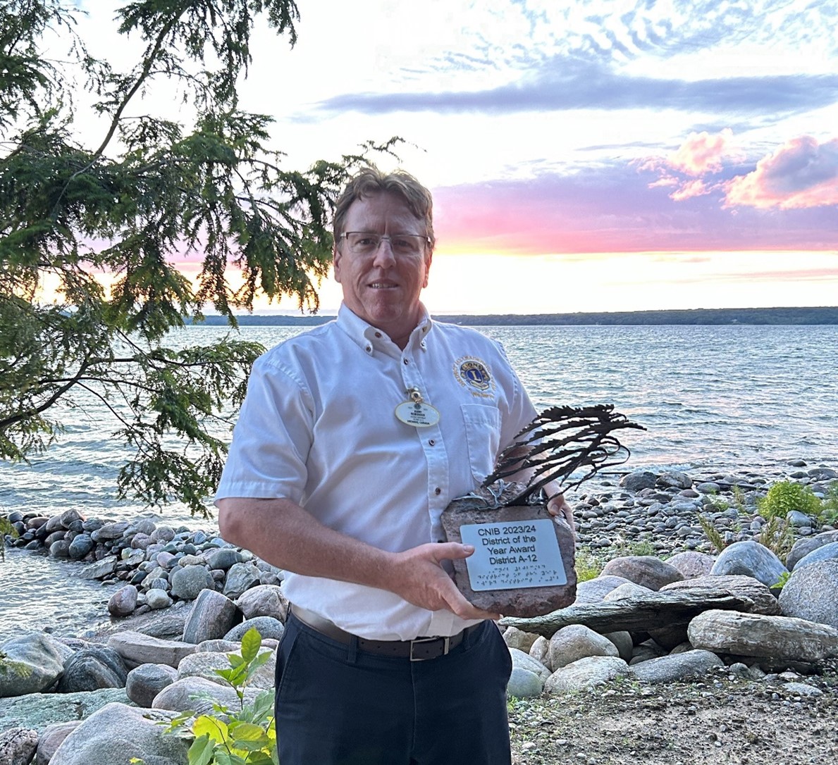 An image of Jerry Rebidoux hold his CNIB award infront of  Lake Joe i
