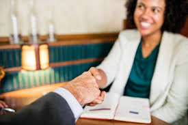 A woman smiles as she shakes a male colleague's hand across a table.