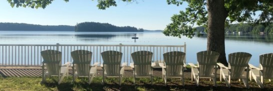 White Muskoka chairs lined up along the lakefront at CNIB Lake Joe.