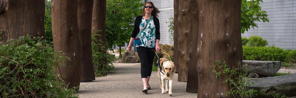 Une femme et son chien-guide vêtu d'un harnais empruntant un sentier dans un parc.