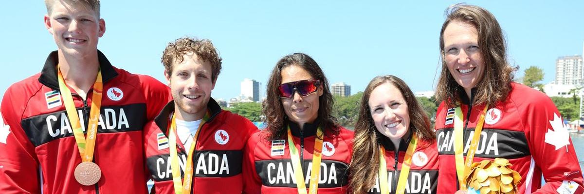 Victoria, en compagnie de deux hommes et de deux femmes, portant une veste de l'Équipe Canada et une médaille de bronze.