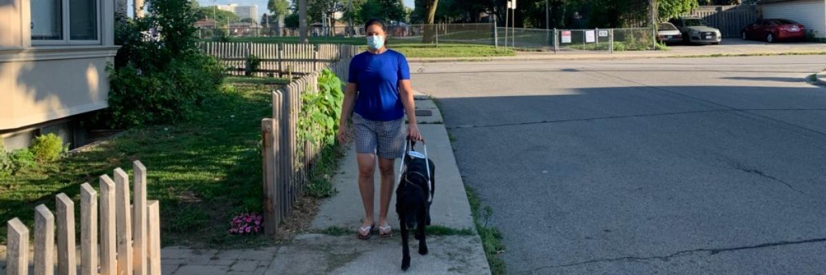 Victoria Nolan et son chien- guide, Alan, marchant sur un trottoir par une journée ensoleillée. Victoria porte un masque facial.