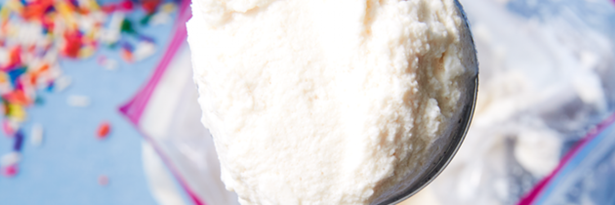 Gros plan d'une cuillère à crème glacée en argent avec une boule de glace à la vanille au-dessus d'un sac de glace à fermeture à glissière avec des paillettes colorées dans un bol sur la gauche.