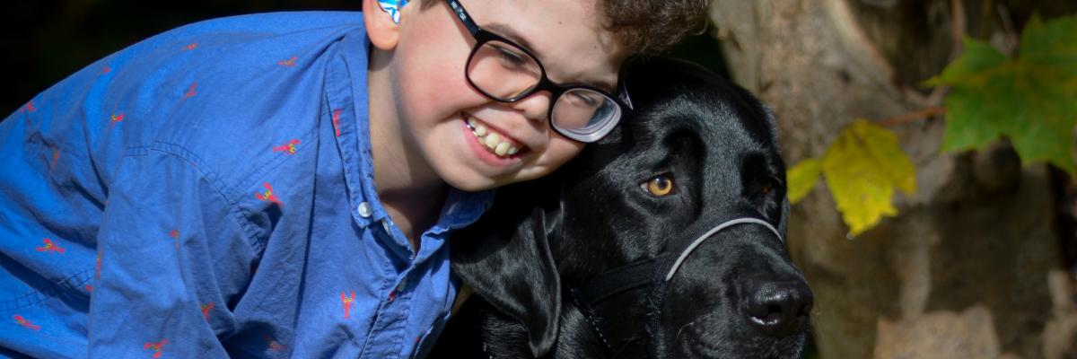 Kaiden, 10 ans, souriant et penché pour embrasser son chien compagnon d’INCA, Flinn, un croisement labrador retriever.